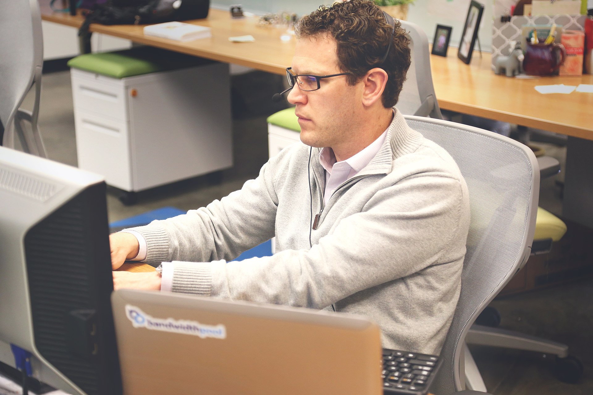A person working at a coworking-style desk with two screens and a laptop