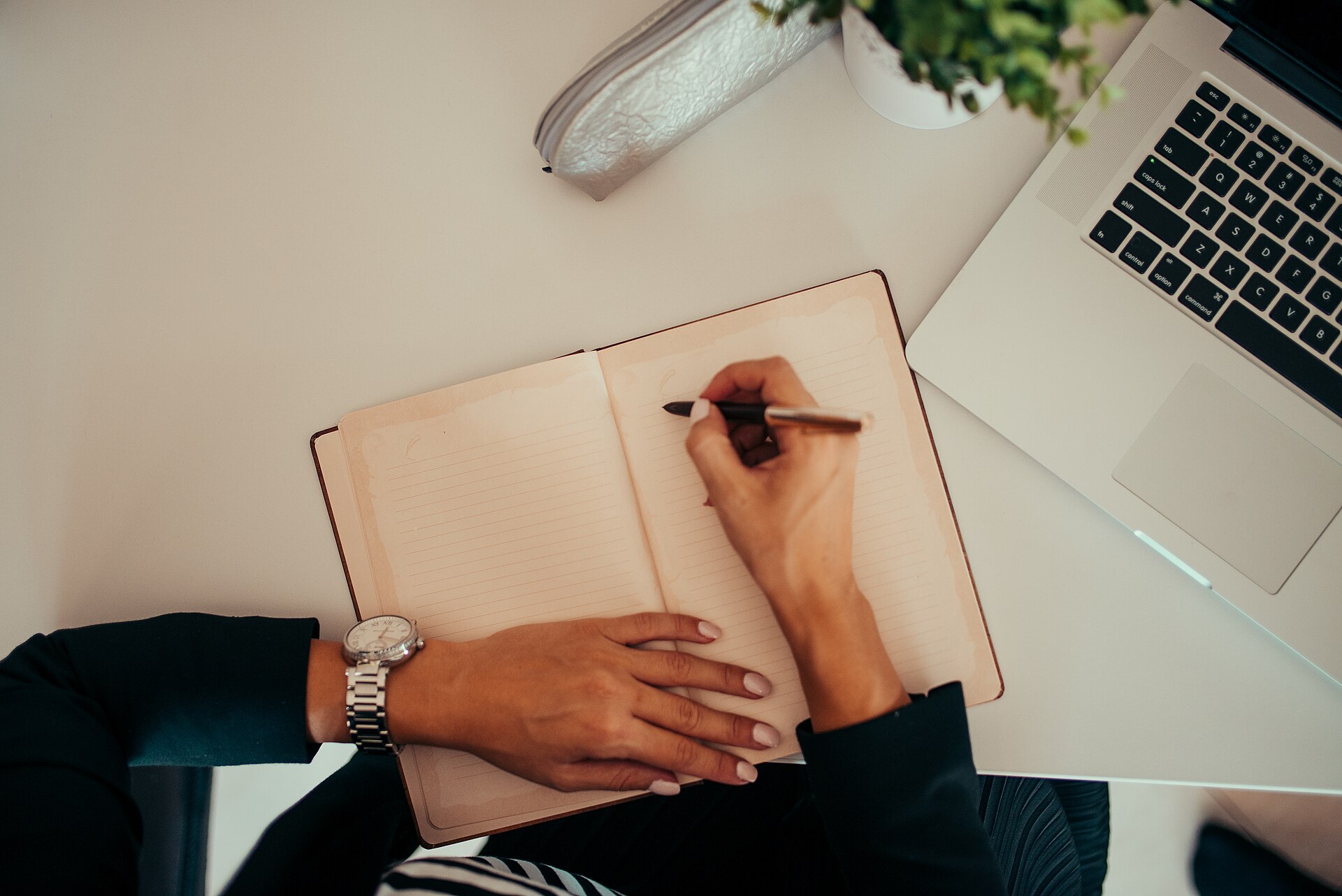 A hand writing in a notebook beside a laptop